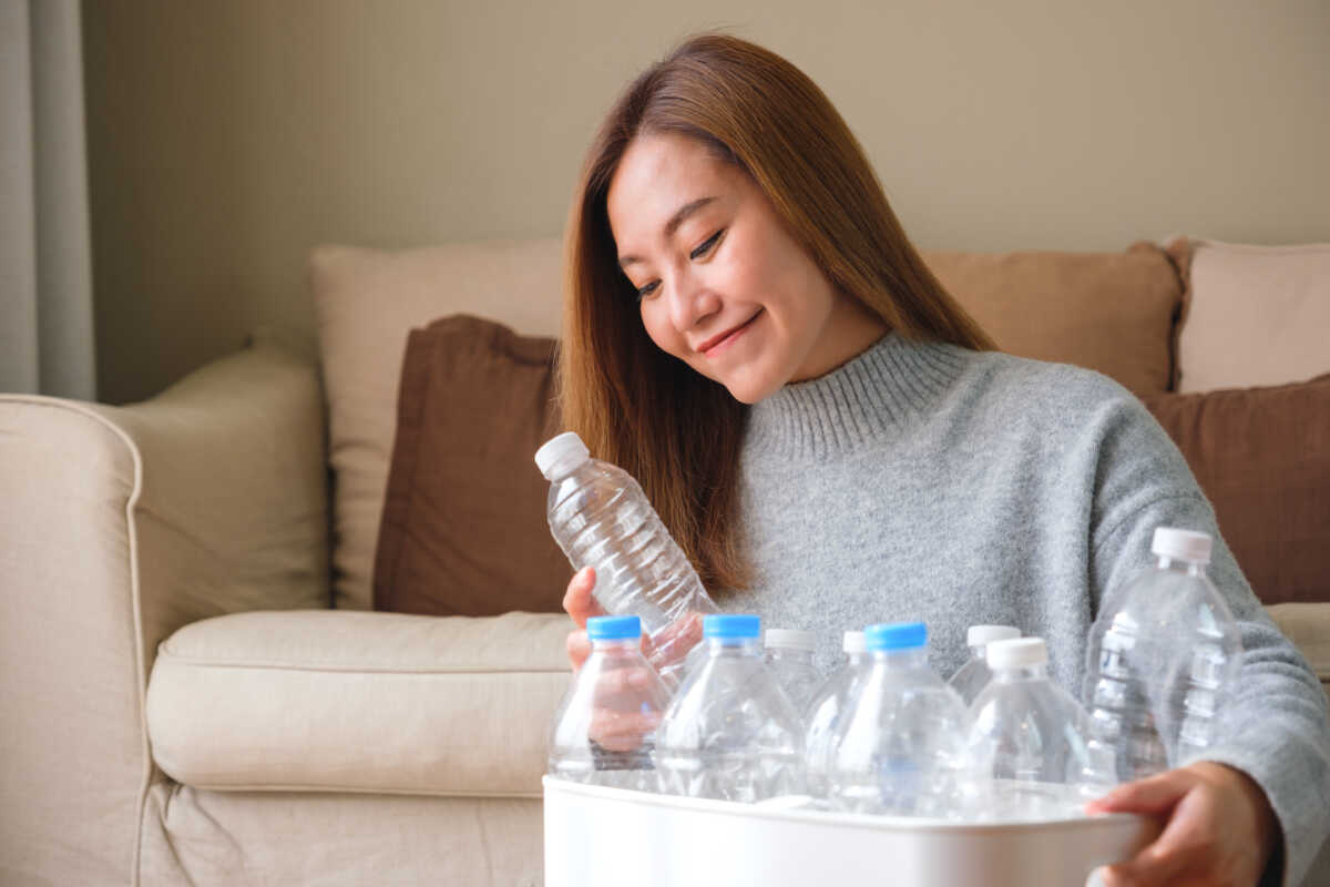 Portrait image of a woman collecting and separating recyclable garbage plastic bottles into a trash bin at home