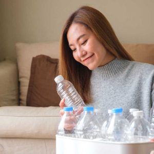 Portrait image of a woman collecting and separating recyclable garbage plastic bottles into a trash bin at home