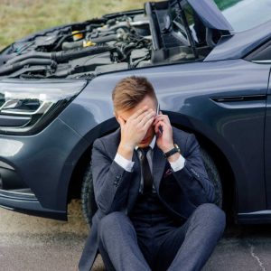 Upset young man use phone sitting on road near the broken car opened the hood help repair stress problem emergency insurance auto